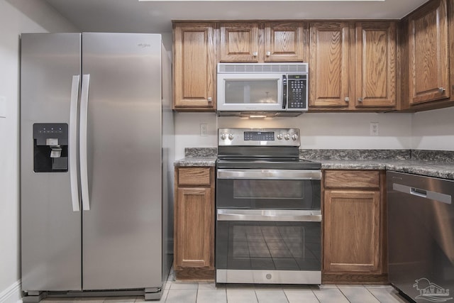 kitchen with stainless steel appliances, dark stone counters, and light tile patterned floors