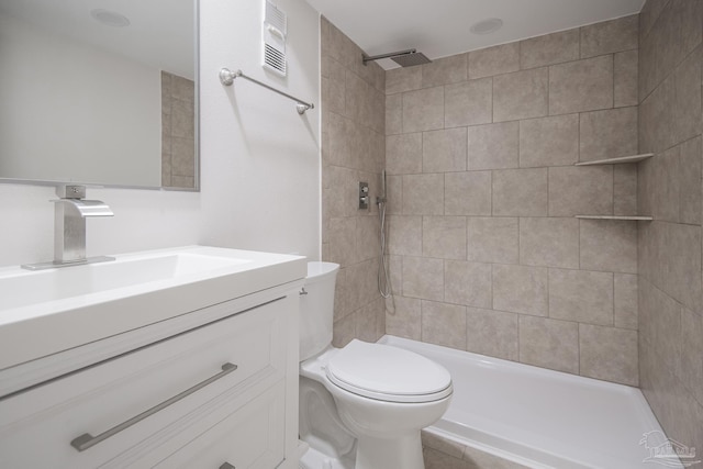 bathroom featuring a tile shower, vanity, and toilet