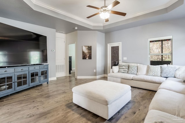 living room featuring a tray ceiling, crown molding, baseboards, and wood finished floors