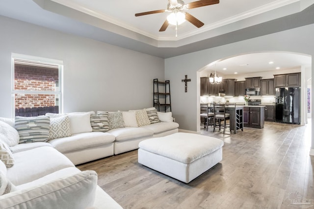 living room featuring light wood-style floors, arched walkways, ornamental molding, and ceiling fan