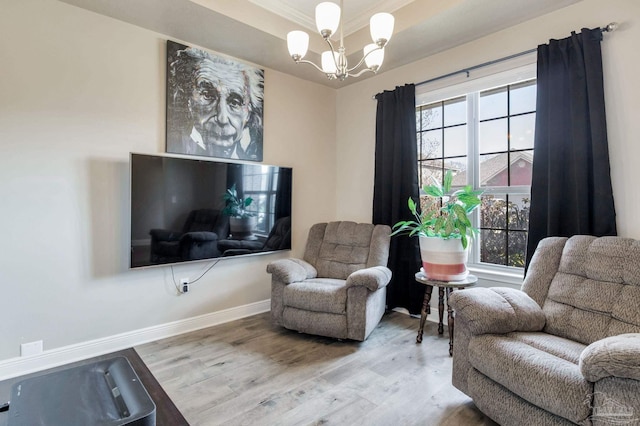 living area with light wood-style floors, baseboards, a chandelier, and a raised ceiling