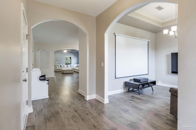 hall with a chandelier, wood finished floors, visible vents, baseboards, and ornamental molding