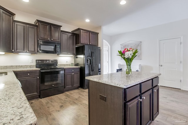 kitchen featuring light wood-type flooring, arched walkways, black appliances, and light stone countertops