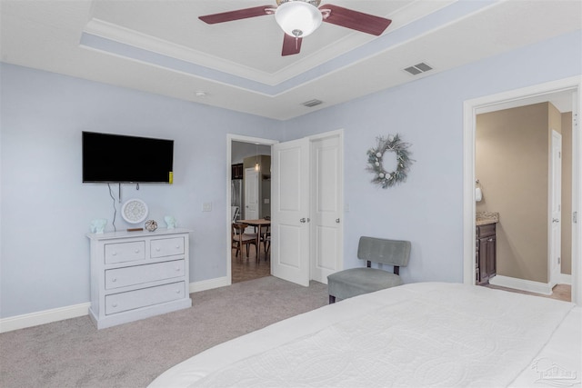 carpeted bedroom with a tray ceiling, ceiling fan, and ensuite bathroom