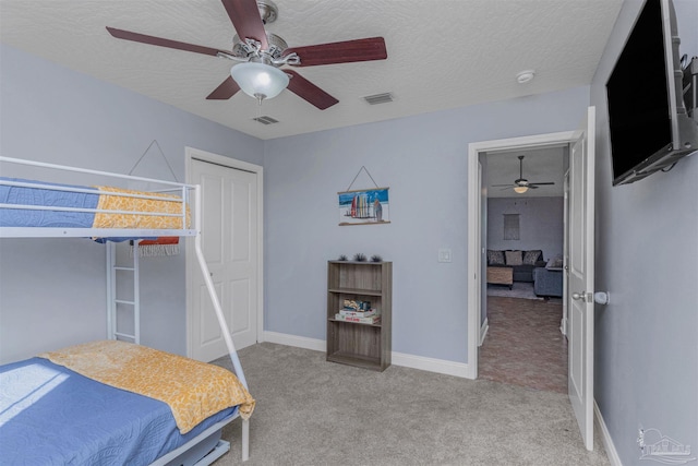 bedroom featuring ceiling fan, light colored carpet, a textured ceiling, and a closet