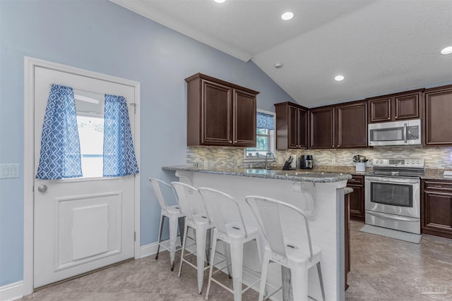 kitchen featuring kitchen peninsula, dark brown cabinets, stainless steel appliances, and vaulted ceiling