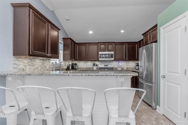 kitchen featuring a kitchen breakfast bar, light stone countertops, kitchen peninsula, and appliances with stainless steel finishes