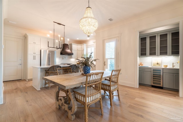 dining room with sink, beverage cooler, ornamental molding, a notable chandelier, and light hardwood / wood-style flooring