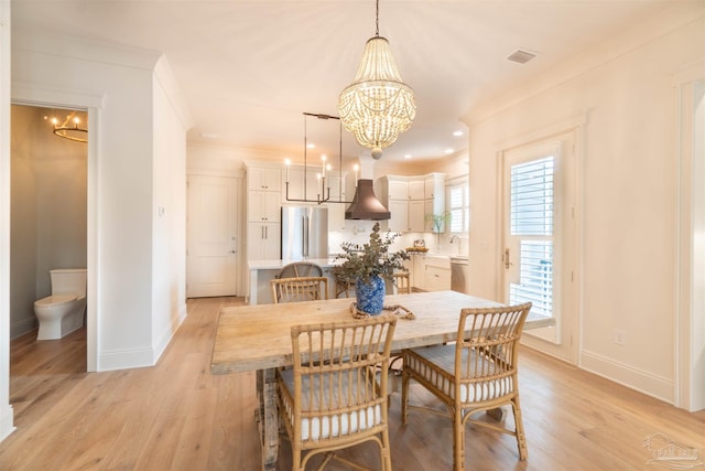 dining area with sink, ornamental molding, light hardwood / wood-style floors, and a chandelier