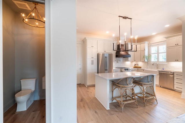 kitchen with a kitchen island, decorative light fixtures, white cabinets, stainless steel appliances, and light wood-type flooring