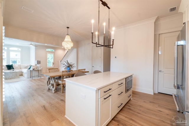 kitchen with appliances with stainless steel finishes, a kitchen island, decorative light fixtures, white cabinets, and light stone counters