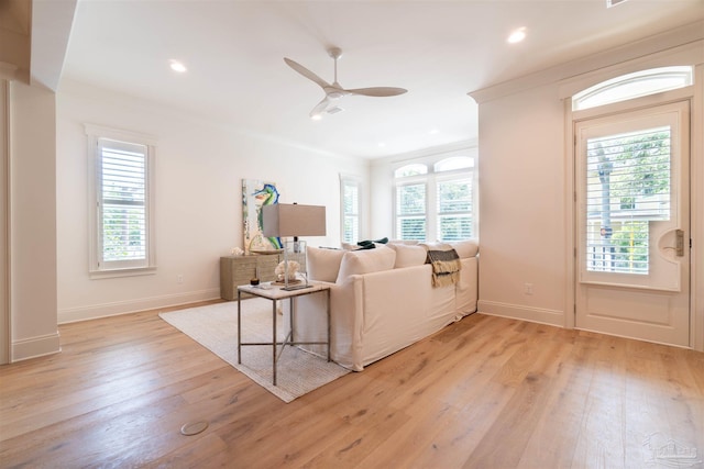 living room featuring plenty of natural light, ornamental molding, ceiling fan, and light wood-type flooring