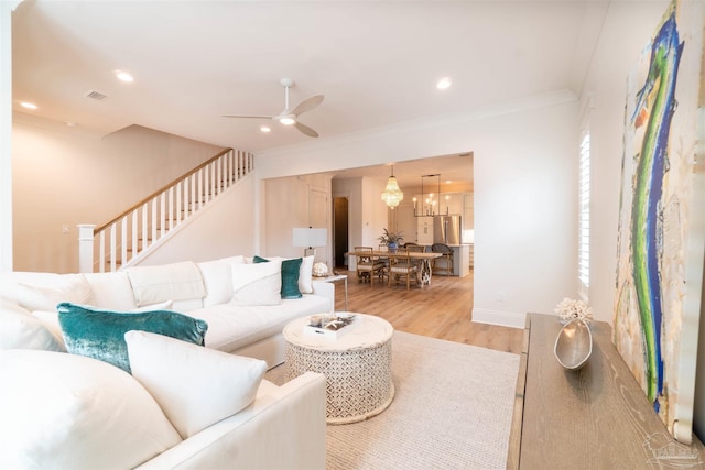 living room featuring ornamental molding, ceiling fan with notable chandelier, and light wood-type flooring