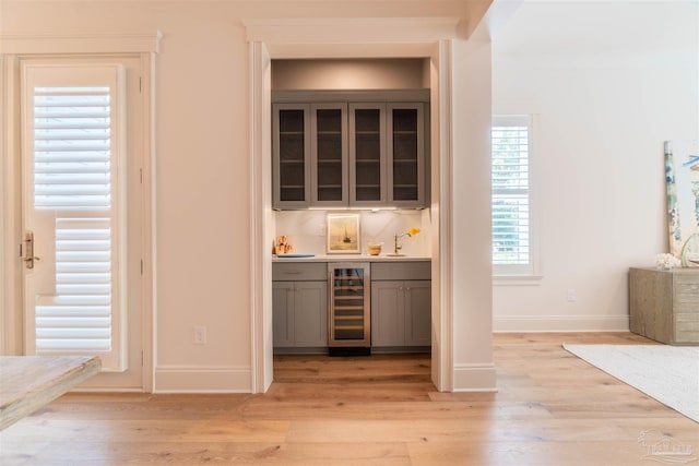 bar with gray cabinets, sink, beverage cooler, and light hardwood / wood-style flooring