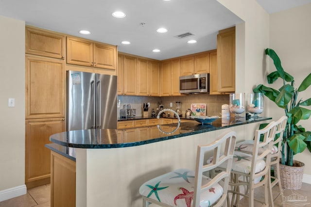 kitchen with dark stone counters, backsplash, appliances with stainless steel finishes, light tile patterned floors, and kitchen peninsula