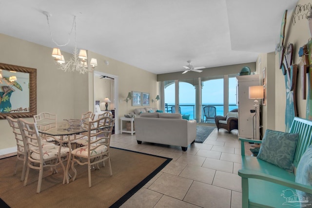 dining space featuring ceiling fan with notable chandelier, a water view, baseboards, and light tile patterned floors