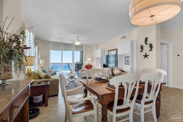 tiled dining room with ceiling fan, a wall of windows, and a textured ceiling