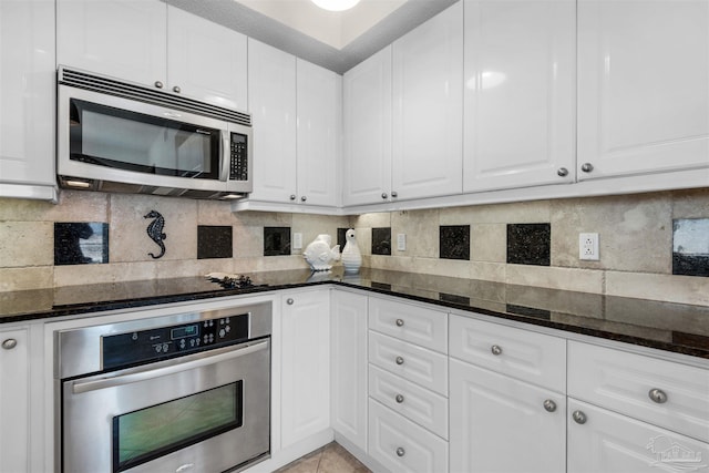 kitchen with stainless steel appliances, dark stone counters, and white cabinets