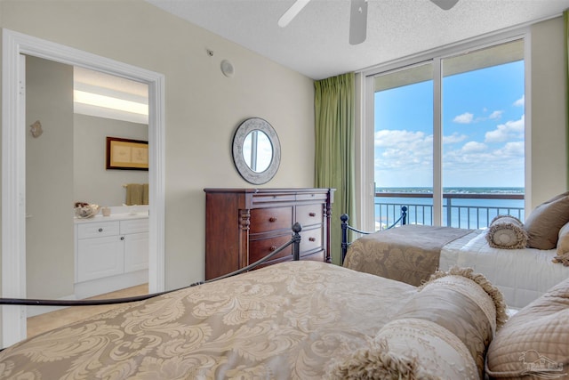 bedroom featuring ensuite bathroom, floor to ceiling windows, a water view, a textured ceiling, and access to outside