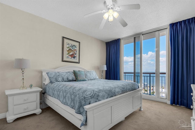 bedroom with access to outside, floor to ceiling windows, a water view, light carpet, and a textured ceiling