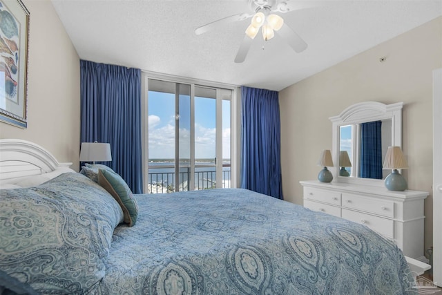 bedroom with a water view, access to outside, a textured ceiling, and ceiling fan