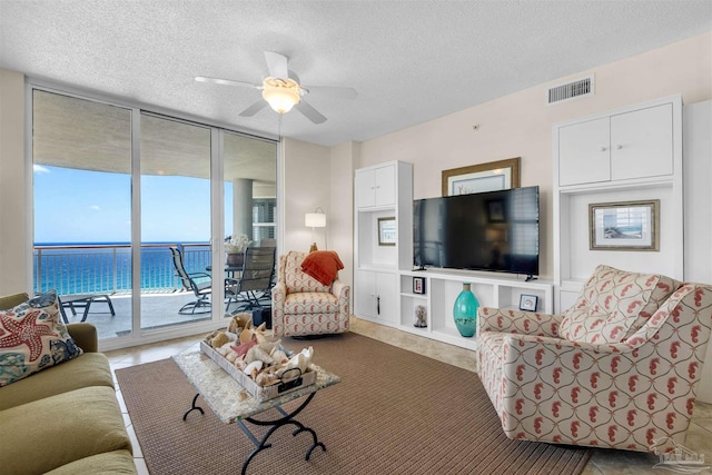 living room featuring a water view, ceiling fan, floor to ceiling windows, and a textured ceiling