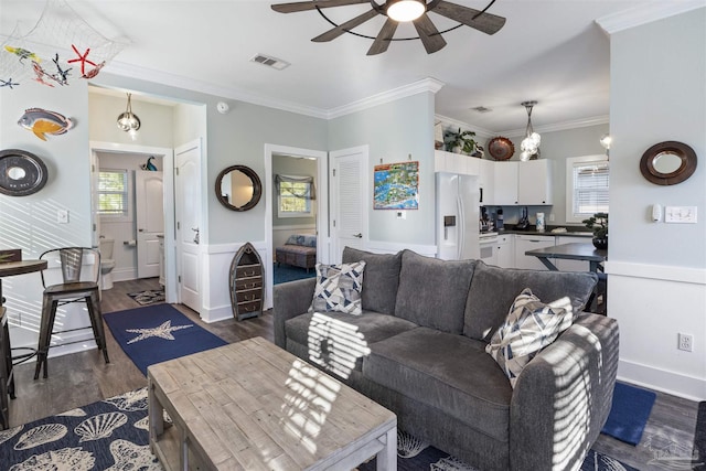 living area with ceiling fan, visible vents, wainscoting, dark wood-style floors, and crown molding