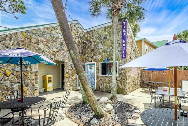 back of house with stone siding, a patio area, fence, and outdoor dining area