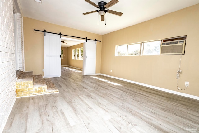 interior space featuring hardwood / wood-style flooring, ceiling fan, brick wall, a wall unit AC, and a barn door