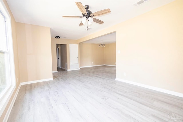 empty room featuring plenty of natural light, ceiling fan with notable chandelier, and light hardwood / wood-style flooring