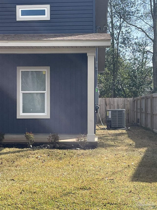 view of side of home with central AC unit, a lawn, and fence