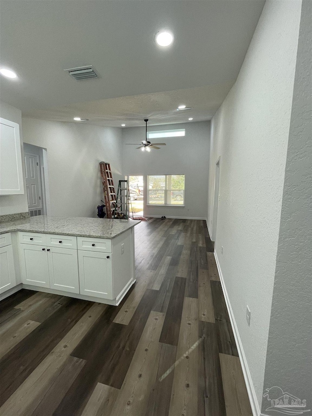 kitchen with light stone countertops, dark wood-style floors, white cabinets, open floor plan, and visible vents