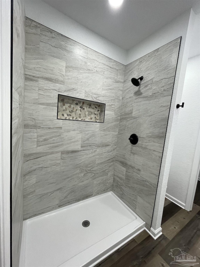 full bath with wood finished floors, baseboards, and a tile shower