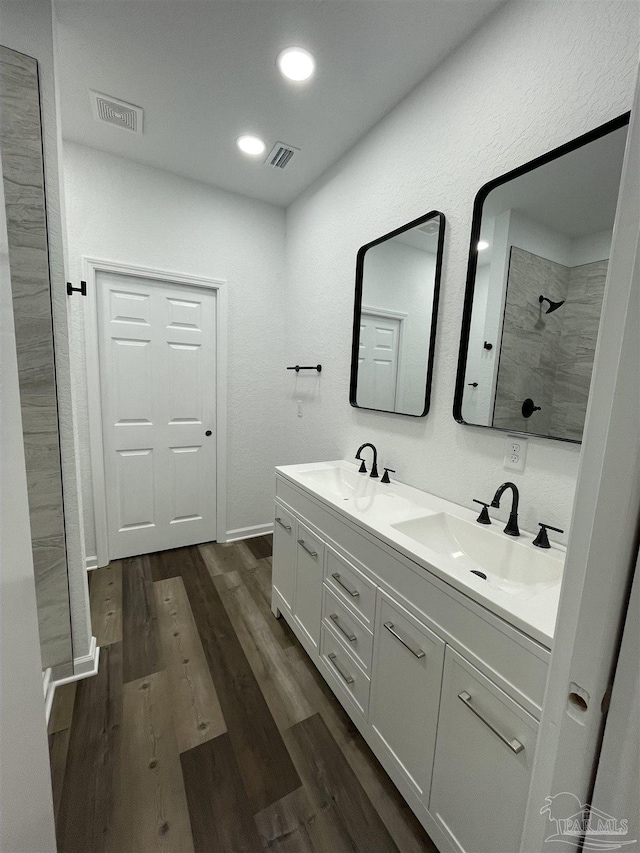 bathroom featuring recessed lighting, a tile shower, wood finished floors, and a sink