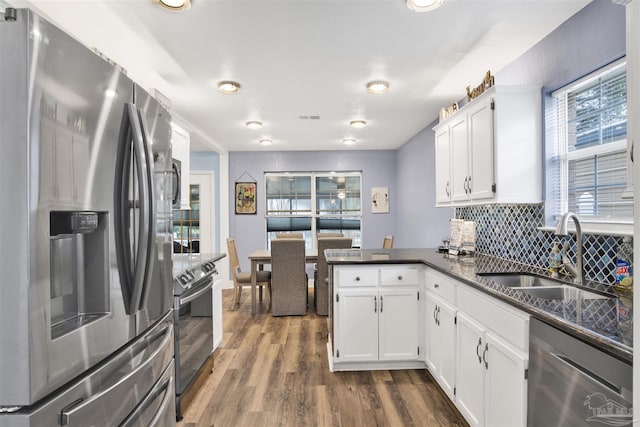 kitchen featuring stainless steel appliances, dark wood-type flooring, white cabinets, a sink, and a peninsula