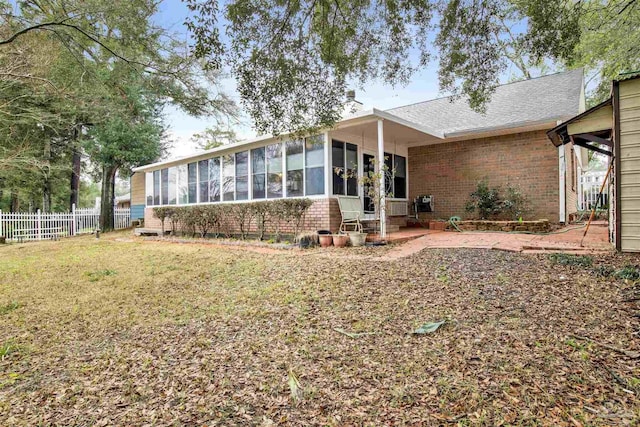 view of front facade featuring a sunroom, fence, a front lawn, and brick siding