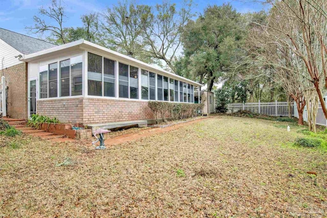 rear view of property featuring a yard, a sunroom, brick siding, and fence