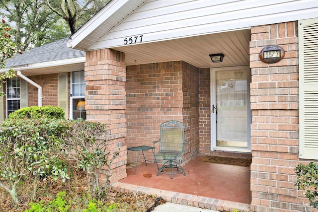 property entrance with a shingled roof and brick siding