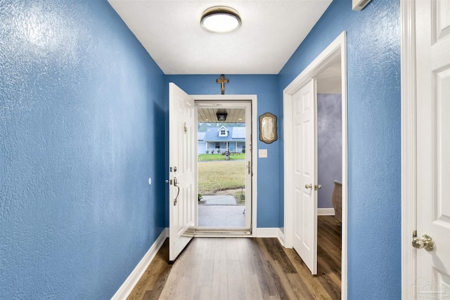 entryway with dark wood-type flooring, a textured wall, and baseboards