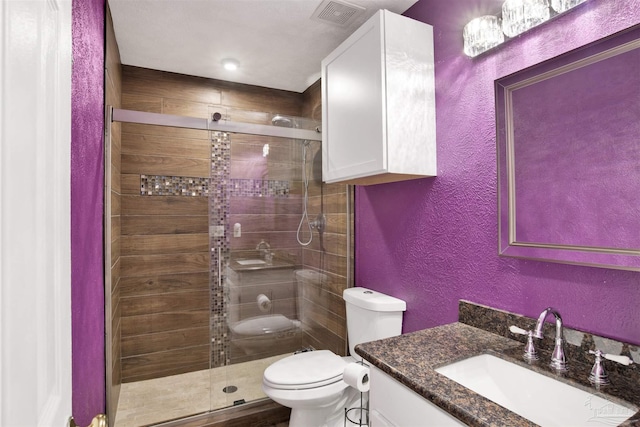 full bathroom featuring a shower stall, a textured wall, vanity, and toilet