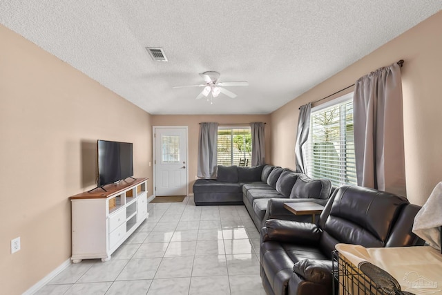 living area with a textured ceiling, light tile patterned flooring, visible vents, baseboards, and a ceiling fan