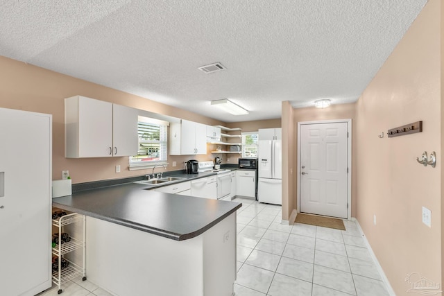 kitchen with a peninsula, white appliances, a sink, white cabinets, and dark countertops