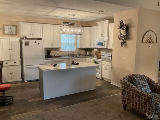 kitchen with white appliances, visible vents, white cabinets, a kitchen island, and a sink