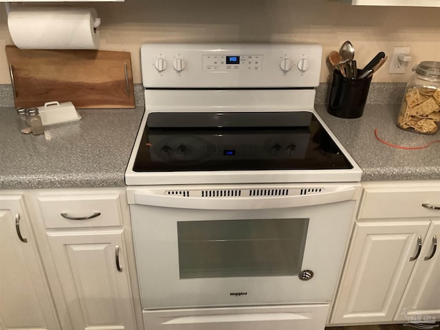 kitchen with electric range, dark countertops, and white cabinetry