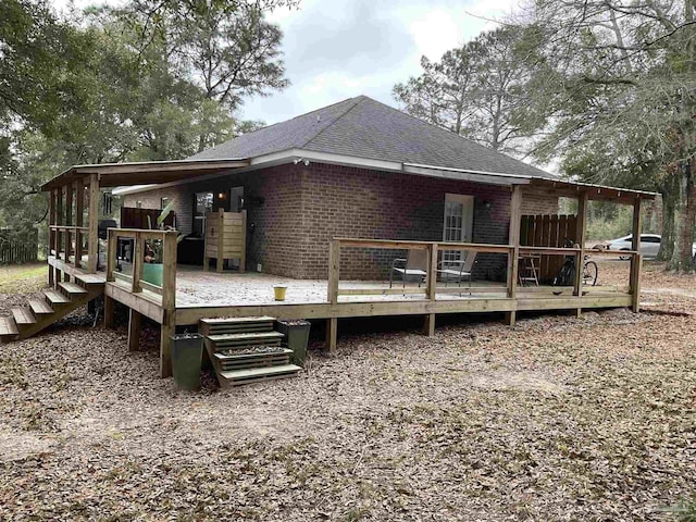 rear view of house with a shingled roof, a deck, and brick siding