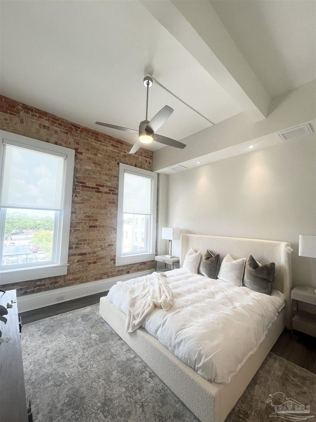 bedroom with multiple windows, brick wall, and wood finished floors