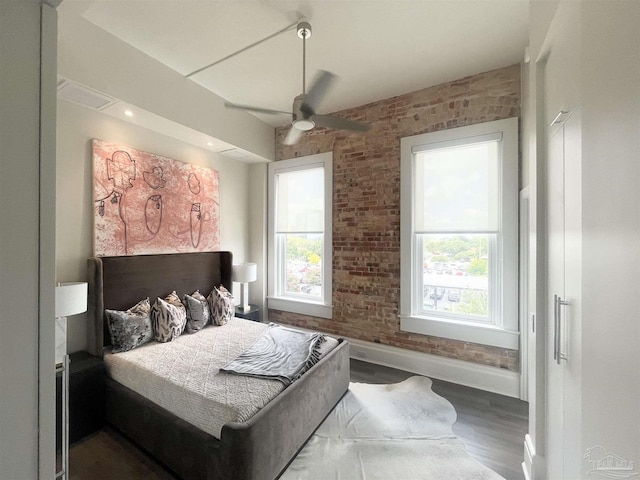 bedroom featuring brick wall, multiple windows, and wood finished floors