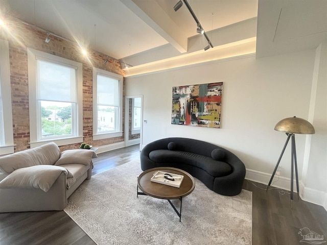 living area with brick wall, wood finished floors, beam ceiling, and baseboards