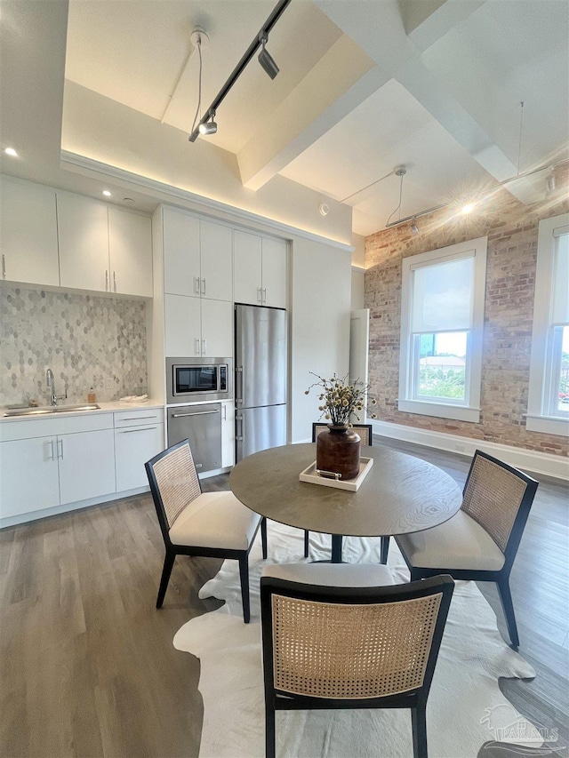 dining room with light wood finished floors, beam ceiling, and track lighting