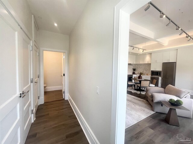 corridor with dark wood-type flooring, track lighting, and baseboards